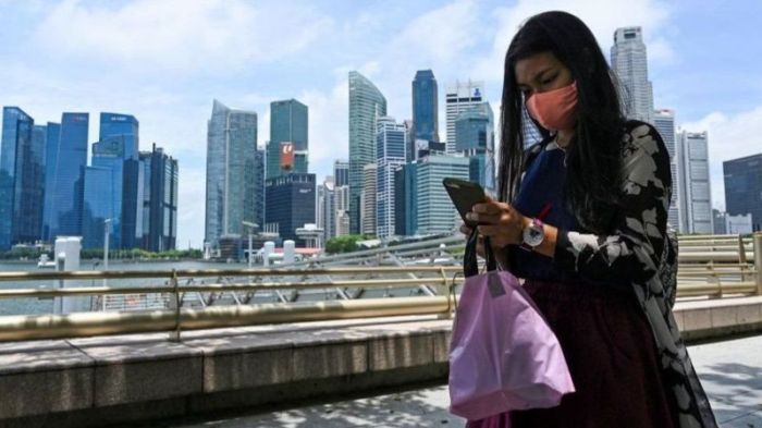 امرأة مستغرقة في تفحص الموبايل أمام عدد من ناطحات السحاب في سنغافورة